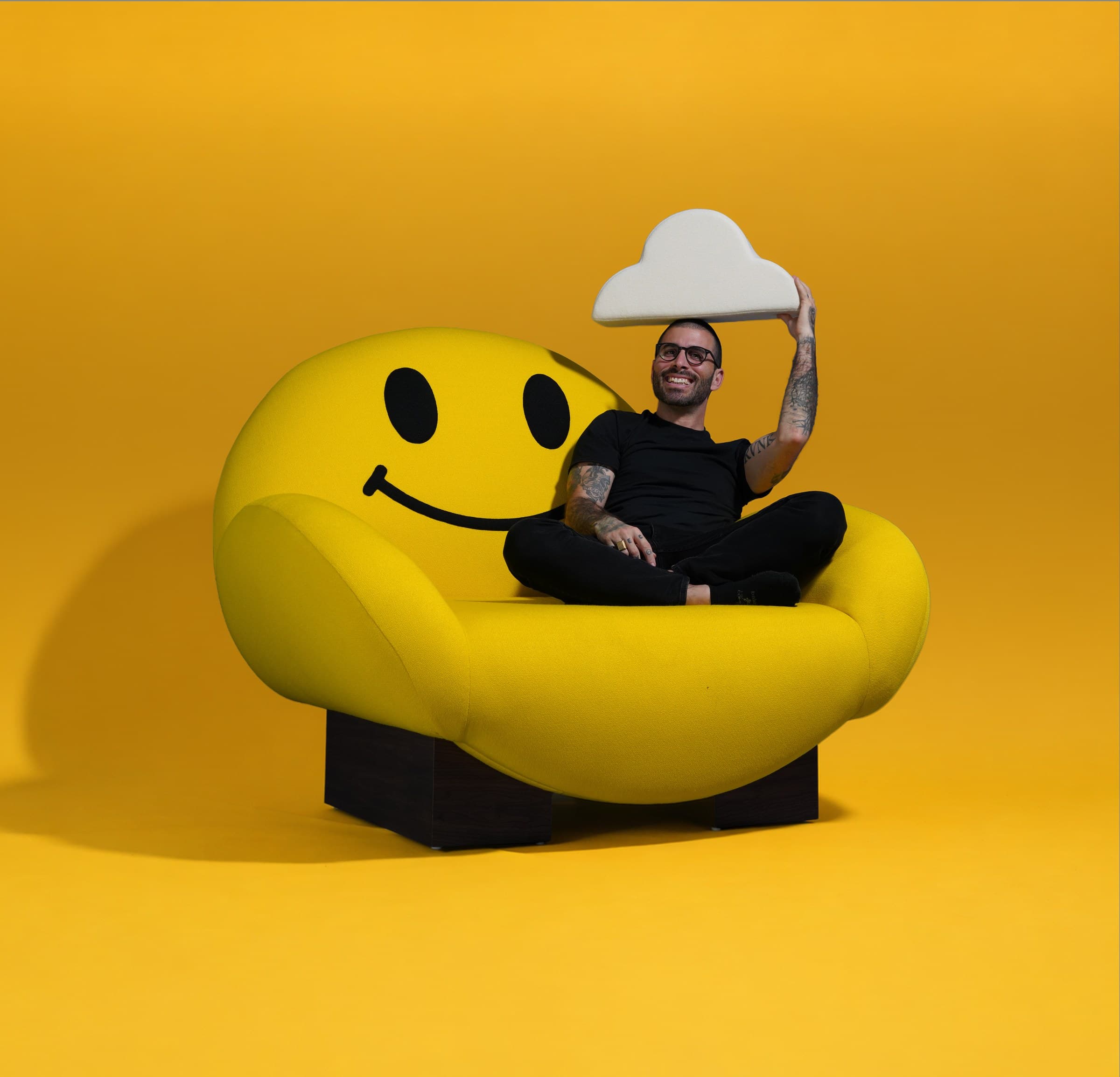 Typoe seated in the Happy Chair holding a cloud pillow against a yellow backdrop